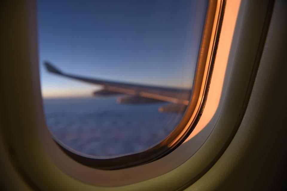 Ventanilla de un avión con el ala sobre las nubes al atardecer